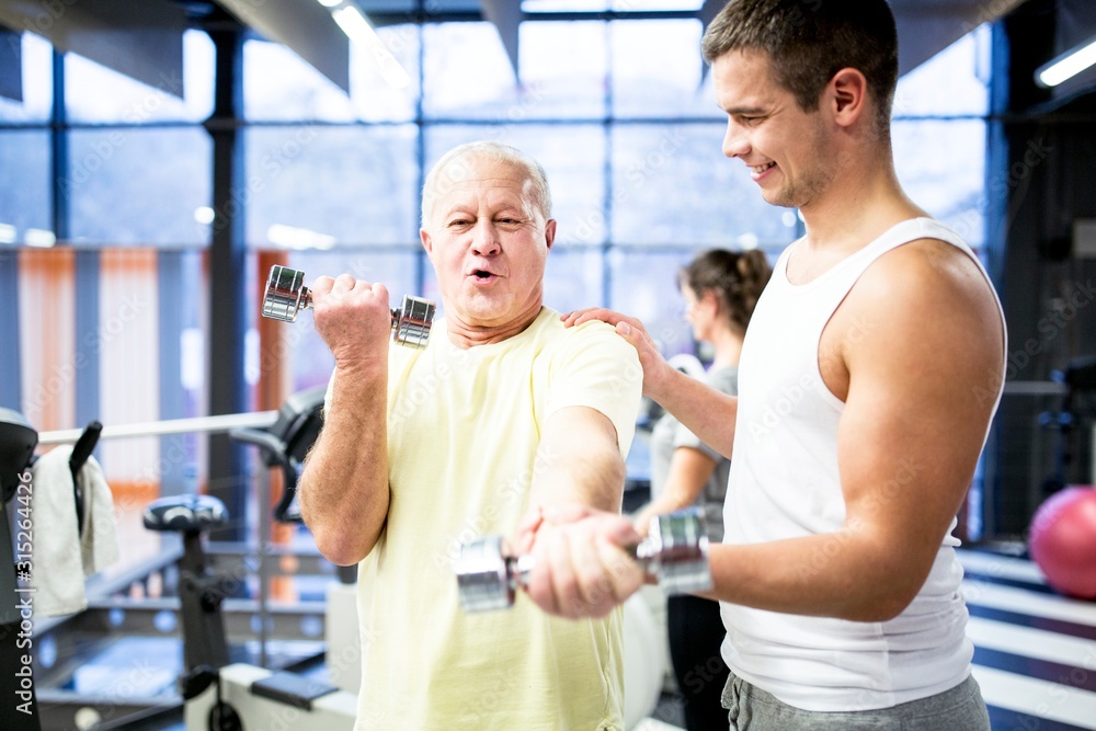 Man holding dumbbell with trainer support Man holding dumbbell with trainer support