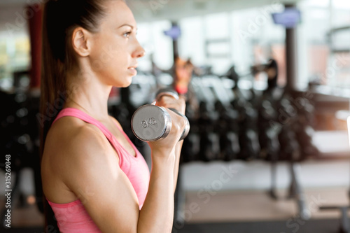 slim beautiful woman wearing pink and black sportswear doing exercise using dumbbells in a gym. sport lifestyle concept