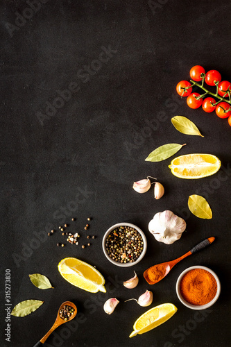 Kitchen frame with spices and food - pepper, garlic, cherry tomatoes - on black background top-down frame copy space