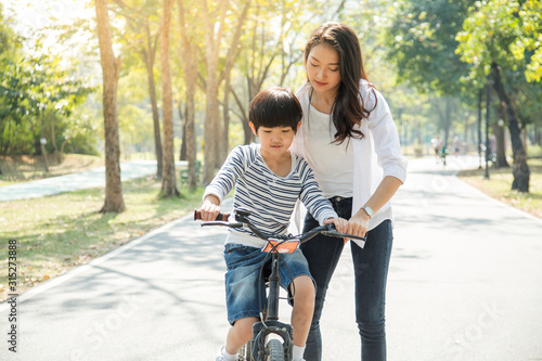 family mom and child concept.Beautiful and happy Asian mother teaching her cute son to ride a bicycle in the Park.