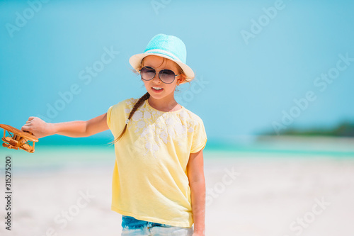 Happy little girl with toy airplane in hands on white sandy beach.