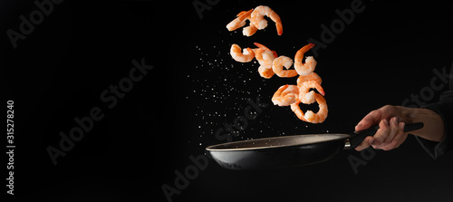 The chef prepares shrimp on a black background, seafood. Cooking, freezing. Banner. With space for advertising a cafe, restaurant, or advertising a seafood market and selling shrimp photo