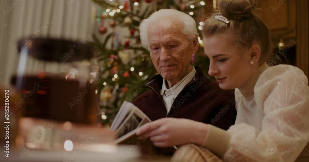 Granddaughter And Grandfather Looking At Photo Album In House Granddaughter And Grandfather Looking At Photo Album In House