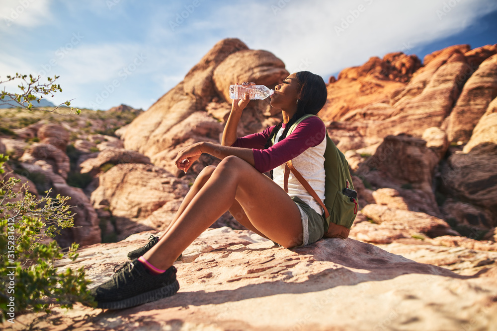 female hiker drinking from water bottle on cliff ledge at red rock canyon