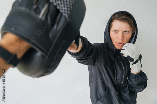 Fighter woman training with trainer. A woman in gloves and a black hoodie hits the trainer's gloves.