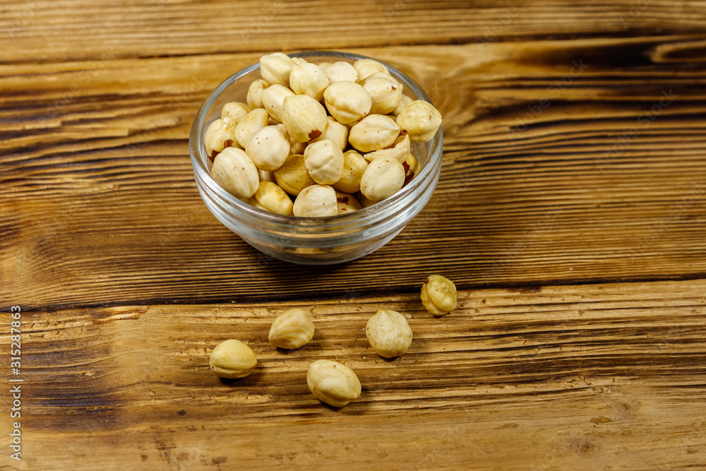 Peeled hazelnuts in glass bowl on wooden table Peeled hazelnuts in glass bowl on wooden table