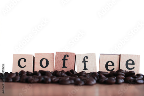 Wooden block with coffee alphabet on pile of coffee beans on wooden table, white background..