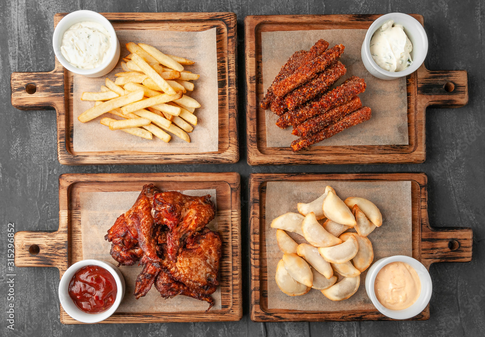 Set of beer snacks. Consisting of chicken wings, french fries, hot carrot sticks and dumplings fries with sauces. . Served on wooden boards. View from above. Gray concrete background. Set of beer snacks. Consisting of chicken wings, french fries, hot carrot sticks and dumplings fries with sauces. . Served on wooden boards. View from above. Gray concrete background.