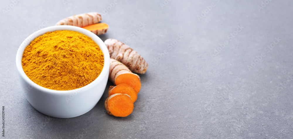 Turmeric root and bowl with turmeric powder on gray texture. Turmeric root and bowl with turmeric powder on gray texture.