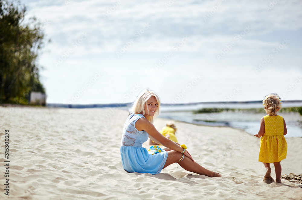 Naklejka premium Happy family relaxing by the sea. Happy family resting at beach in summer.Young mother and her adorable little daughters on beach vacation. Concept of summer,childhood and leisure