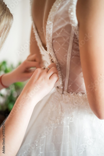 bride's morning. Girlfriend helps put on a dress. Photo from the back. Lacing corset