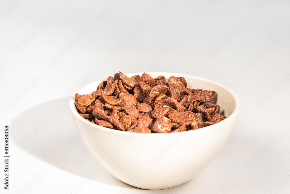 Chocolate corn flakes falling to the white bowl isolated on white. Motion. Chocolate corn flakes falling to the white bowl isolated on white. Motion.