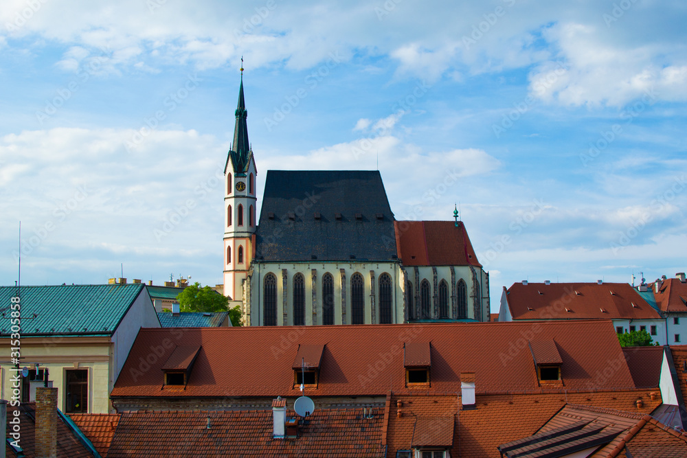 Fototapeta premium Facade of St. Vitus Church with a lot of roofs of houses at the foreground in Cesky Krumlov, Czech Republic