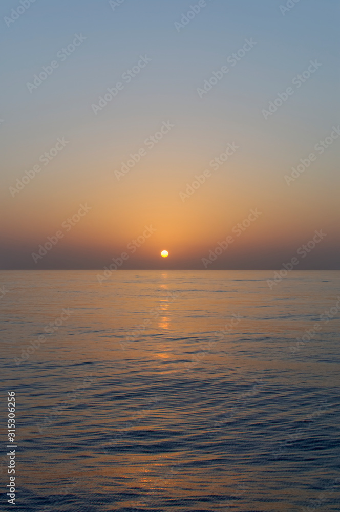 Sunset across calm water as the sun starts to dip over the horizon as a Vessel transits through the Bay of Benin in West Africa,