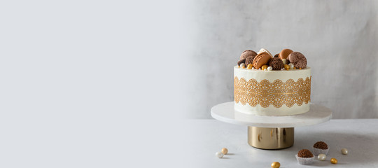 Confectionery, bakery banner. Festive cake decorated with chocolate candies and macaroons on the stand on gray background. Copy space