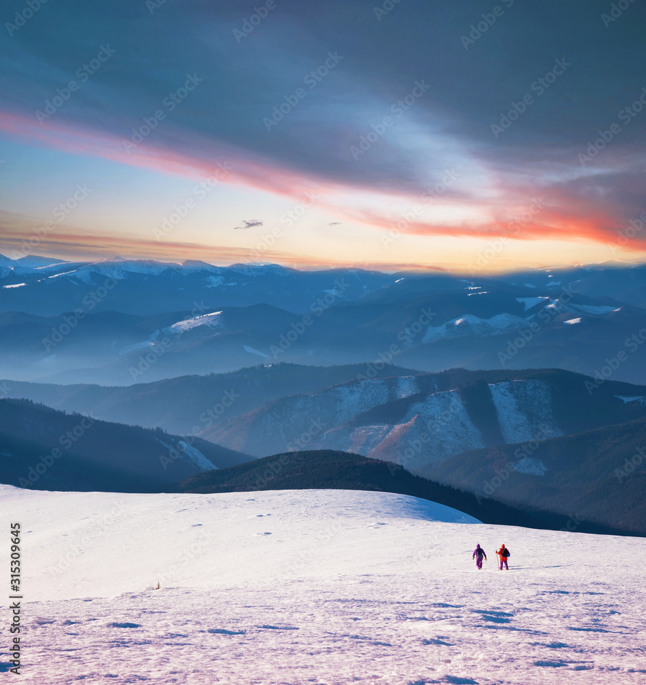 Mystical landscape with two travelers in the winter mountains at sunset