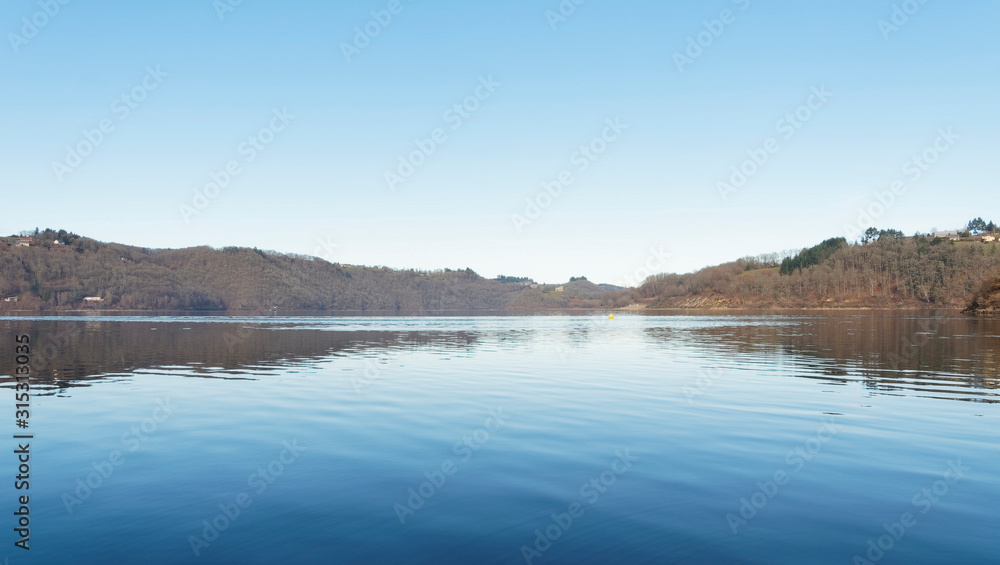 Vue sur les eaux calmes du grand lac de Bort-les-Orgues et ses berges au bord de la Commune de Lanobre
