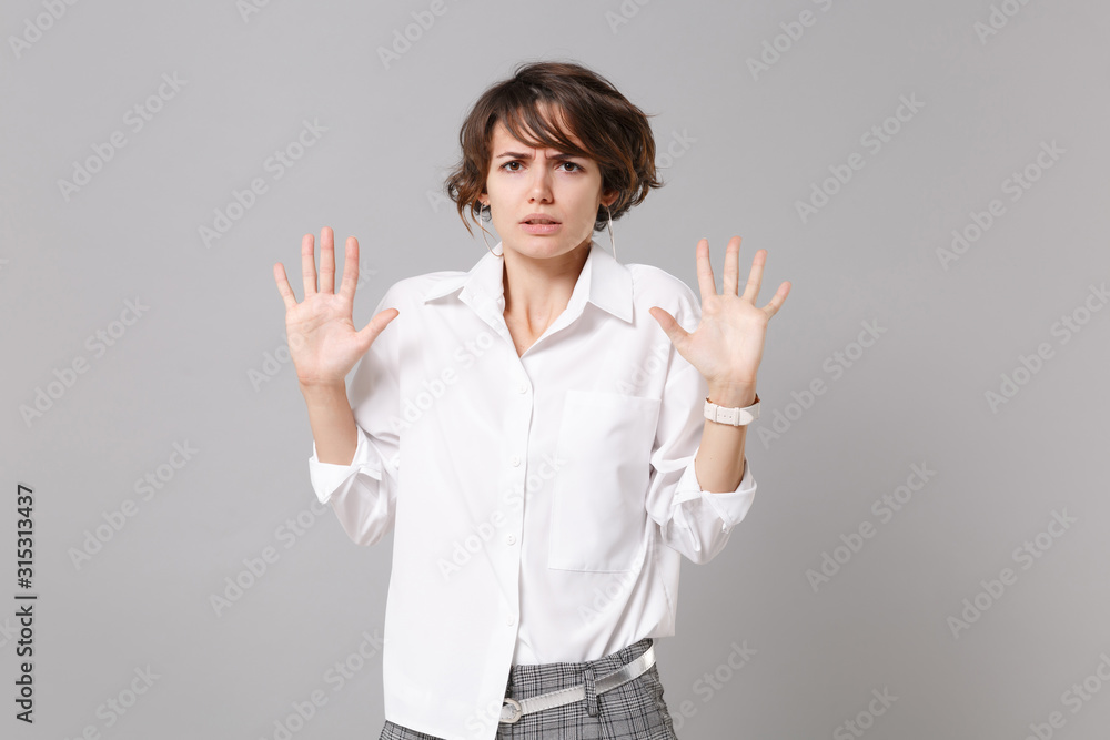 Concerned bewildered young business woman in white shirt posing isolated on grey background in studio. Achievement career wealth business concept. Mock up copy space. Rising hands up, showing palms. Concerned bewildered young business woman in white shirt posing isolated on grey background in studio. Achievement career wealth business concept. Mock up copy space. Rising hands up, showing palms.