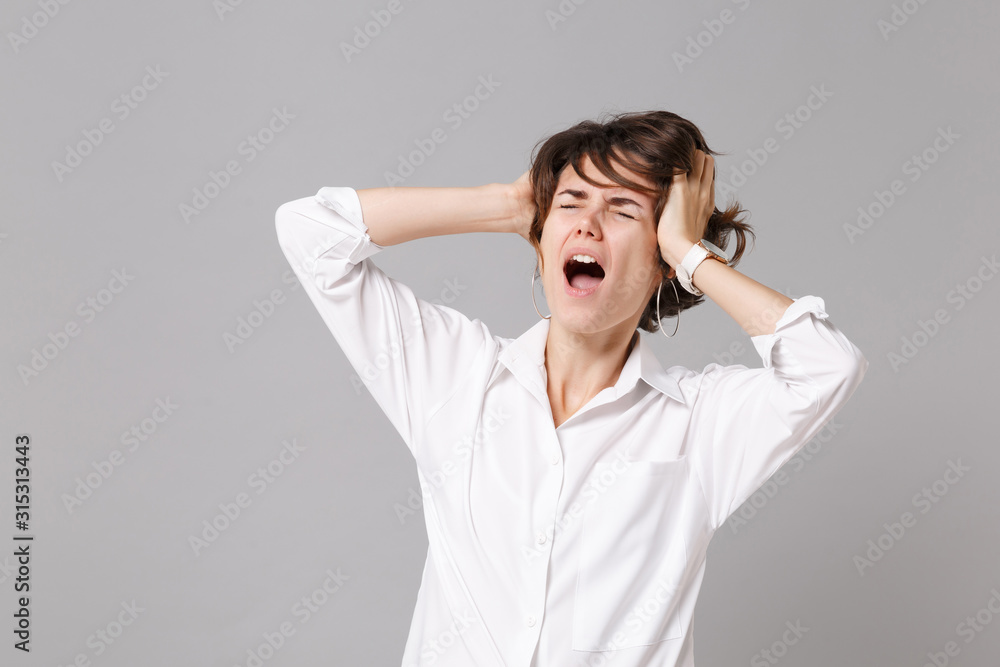 Crazy young business woman in white shirt posing isolated on grey wall background. Achievement career wealth business concept. Mock up copy space. Screaming, keeping eyes closed, put hands on head. Crazy young business woman in white shirt posing isolated on grey wall background. Achievement career wealth business concept. Mock up copy space. Screaming, keeping eyes closed, put hands on head.