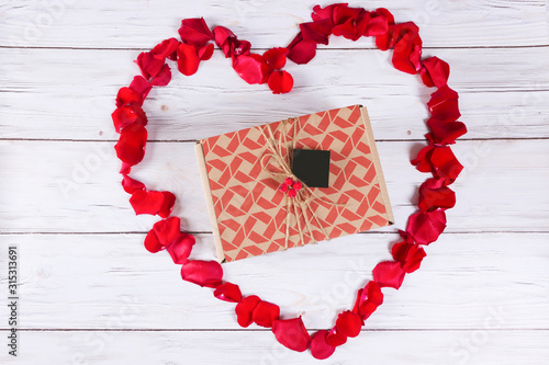 The heart symbol is lined with red rose petals on a light gray wooden background.