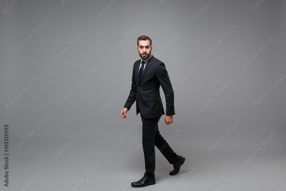 Side view of confident young bearded business man in classic black suit shirt tie posing isolated on grey background. Achievement career wealth business concept. Mock up copy space. Looking camera. Side view of confident young bearded business man in classic black suit shirt tie posing isolated on grey background. Achievement career wealth business concept. Mock up copy space. Looking camera.