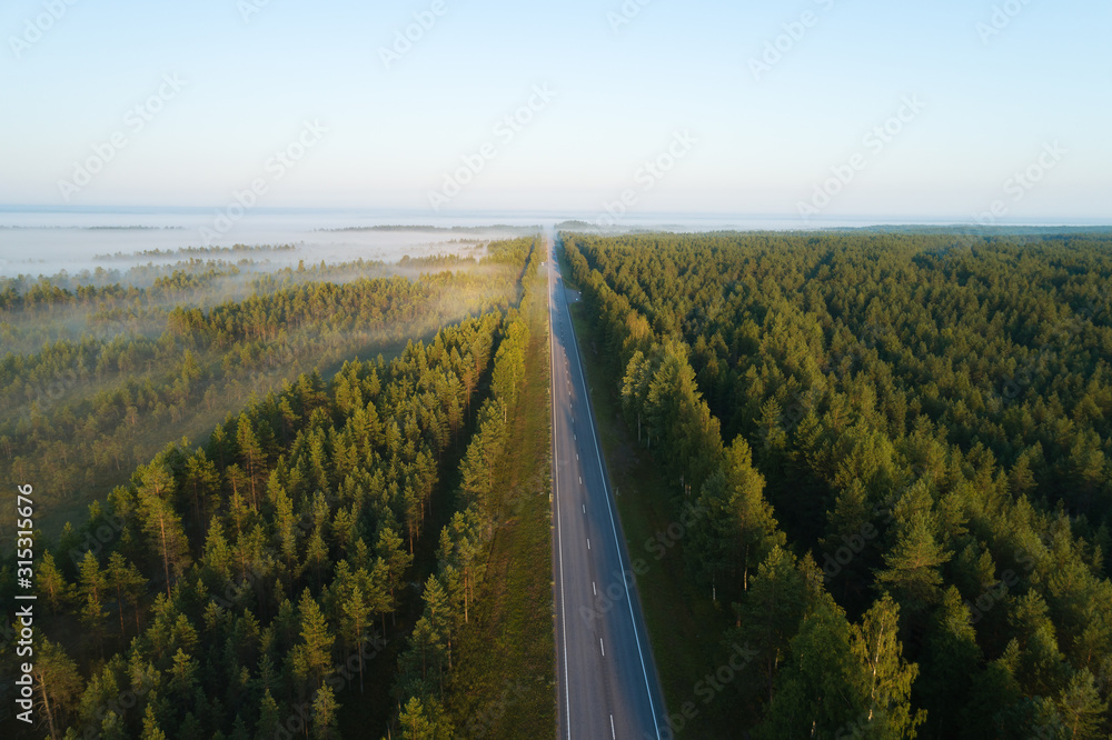 Straight road in  the morning view from above. Transportation background. Beautiful aerial landscape with road in colorful fog. Misty summer nature.