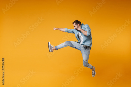 Side view of crazy young bearded man in casual blue shirt posing isolated on yellow orange background studio portrait. People sincere emotions lifestyle concept. Mock up copy space. Jumping, fighting. photo