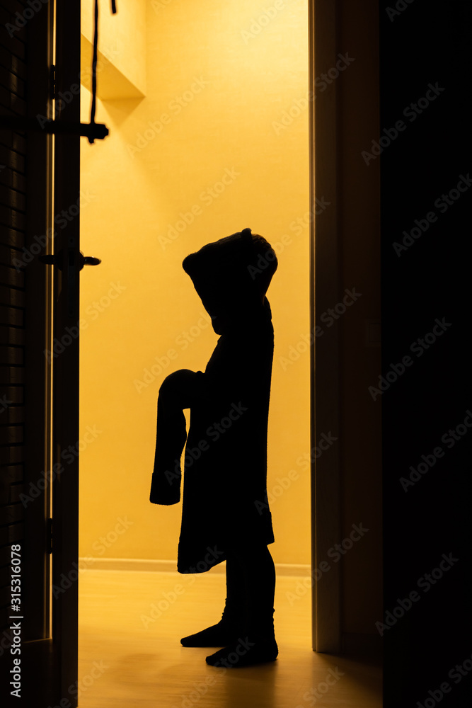 A silhouette of a child in his father's sweater plays a ghost at home. Children silhouettein in the orange light.