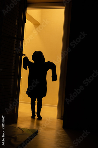A silhouette of a child in his father s sweater plays a ghost at home. Children silhouettein in the orange light.