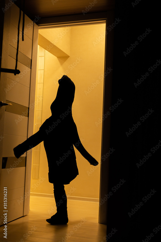 A silhouette of a child in his father's sweater plays a ghost at home. Children silhouettein in the orange light.