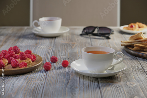 Morning tea for breakfast  puff pastry with and jam  raspberry  with various fruit on the background.    hocolate candy  sunglasses  brown-gray wooden table