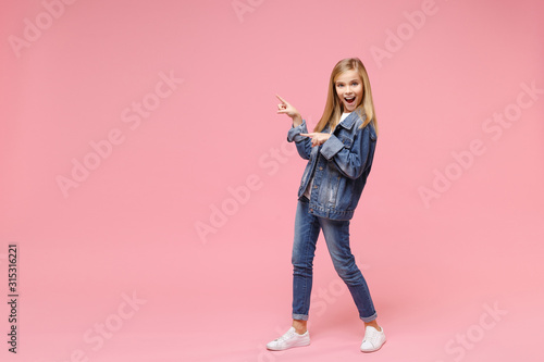 Excited little blonde kid girl 12-13 years old in denim jacket isolated on pastel pink background children studio portrait. Childhood lifestyle concept. Mock up copy space. Point index fingers aside.