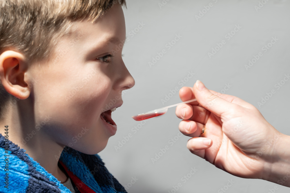 Mother giving boy medicine, cough syrup on a spoon. Sick kid Mother giving boy medicine, cough syrup on a spoon. Sick kid