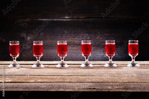 Set of alcoholic cherry cocktails in shot glasses on old wooden plank. Rustic background with vodka in shooters.