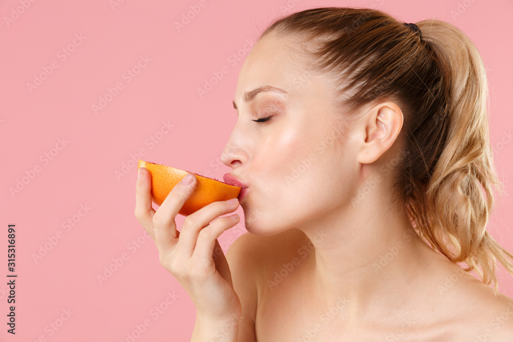 Close up blonde half naked woman 20s perfect skin nude make up blue eyes hold in hand grapefruit isolated on pastel pink background studio portrait. Skin care healthcare cosmetic procedures concept. Close up blonde half naked woman 20s perfect skin nude make up blue eyes hold in hand grapefruit isolated on pastel pink background studio portrait. Skin care healthcare cosmetic procedures concept.