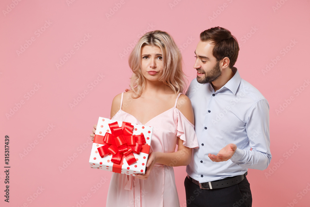 Confused young couple two guy girl in party outfit celebrating posing isolated on pastel pink background. Valentine's Day Women's Day birthday holiday concept. Hold present box with gift ribbon bow. Confused young couple two guy girl in party outfit celebrating posing isolated on pastel pink background. Valentine's Day Women's Day birthday holiday concept. Hold present box with gift ribbon bow.