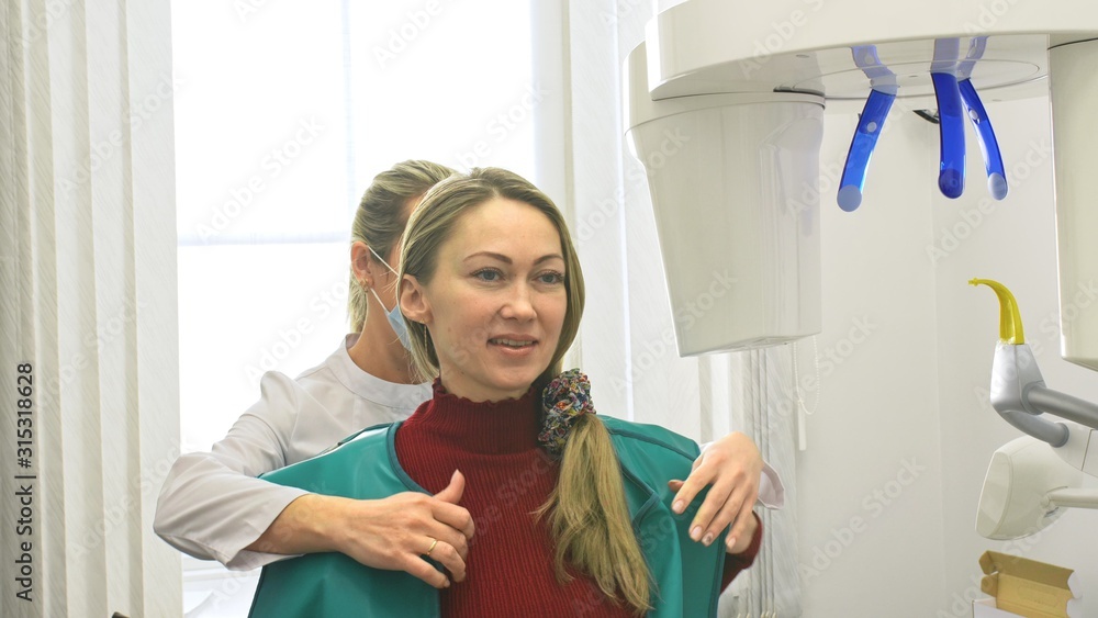 Doctor to take a image 3d scanner tomography of teeth and jaw in modern laboratory dental clinic. Female nurse shows the patient woman an x-ray machine 3d digital scanner. Computer dental diagnostics. Doctor to take a image 3d scanner tomography of teeth and jaw in modern laboratory dental clinic. Female nurse shows the patient woman an x-ray machine 3d digital scanner. Computer dental diagnostics.