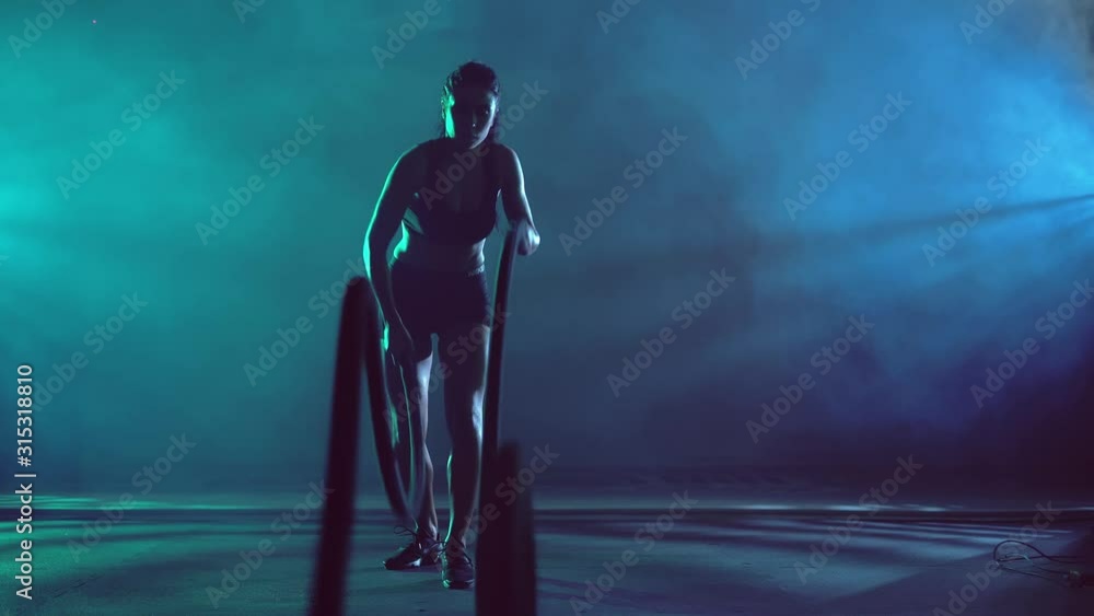 Muscular brunette woman doing battle rope training. Muscular brunette woman doing battle rope training.