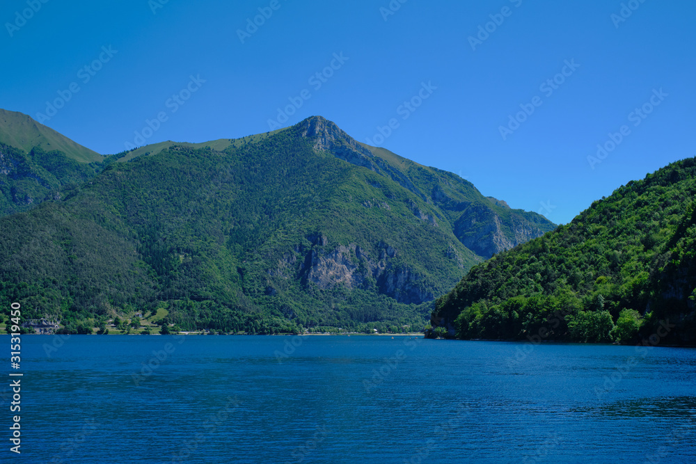 Panoramic view of the lake Ledro. Blue lake, green mountains, blue sky