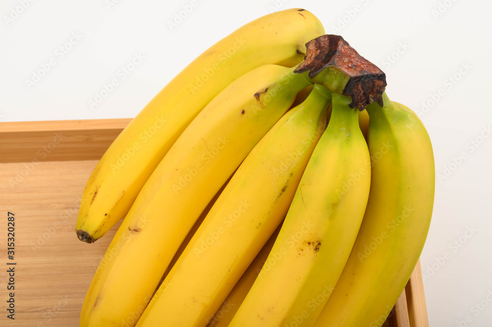 A bunch of ripe yellow bananas on a wooden tray on a white background. Close up.