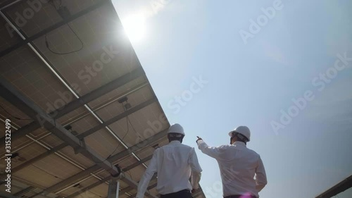 Technician and investor walking in Solar cell Farm through field of solar panels checking the panels at solar energy installation.Solar cells will be an important renewable energy of the future.