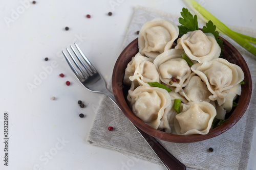 Boiled dumplings with feathers of green onions. In the background are greens, red peppers and bay leaves. In a transparent bowl sour cream.
