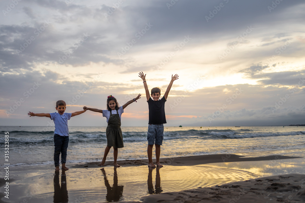 Fototapeta premium Three kids on a beach at sunset