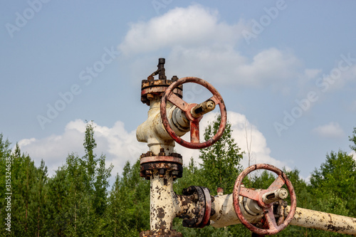 old oil well valve on the background of clouds and forest