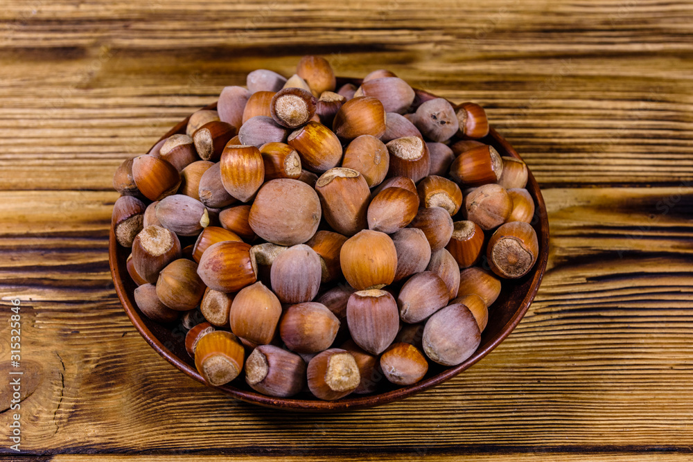 Plate with pile of hazelnuts on a wooden table Plate with pile of hazelnuts on a wooden table