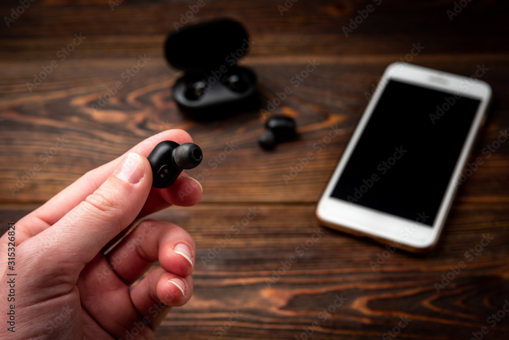 Fototapeta premium Black wireless headphones and mobile phone on dark wooden background.