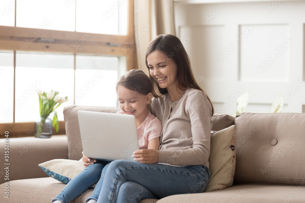 Fototapeta premium Happy mother and preschool daughter using laptop together at home