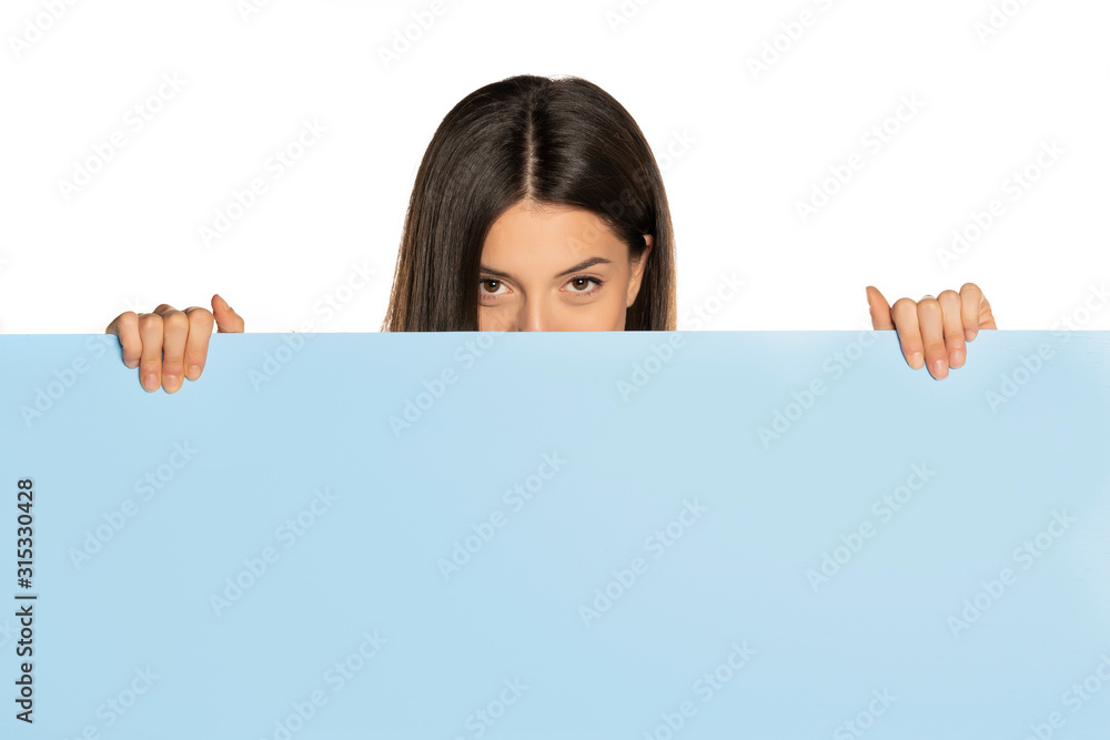young beautiful woman peeking behind a blue empty board young beautiful woman peeking behind a blue empty board