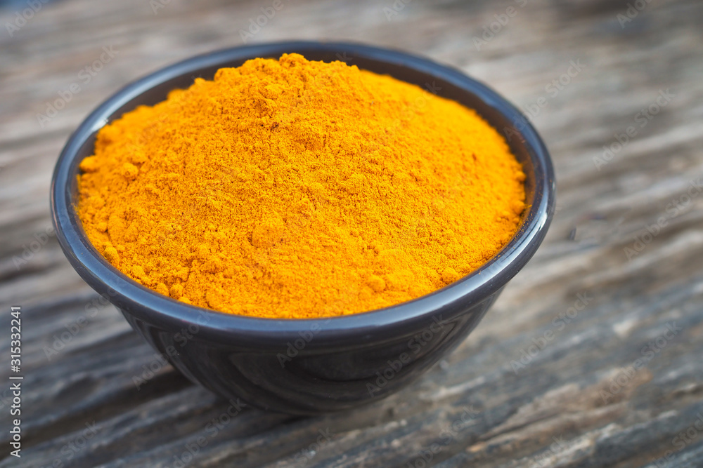 turmeric powder in black bowl on old wooden table background. herbal turmeric powder in black bowl on old wooden table background. herbal