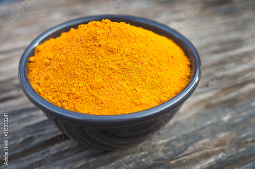 turmeric powder in black bowl on old wooden table background. herbal